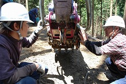 この機械は集材ではスイングヤーダのアームとなり、作業路開設時にヘッドのグラップル付きバケットが威力を発揮。斎藤久義さん（右）が若い社員を現場で指導する
